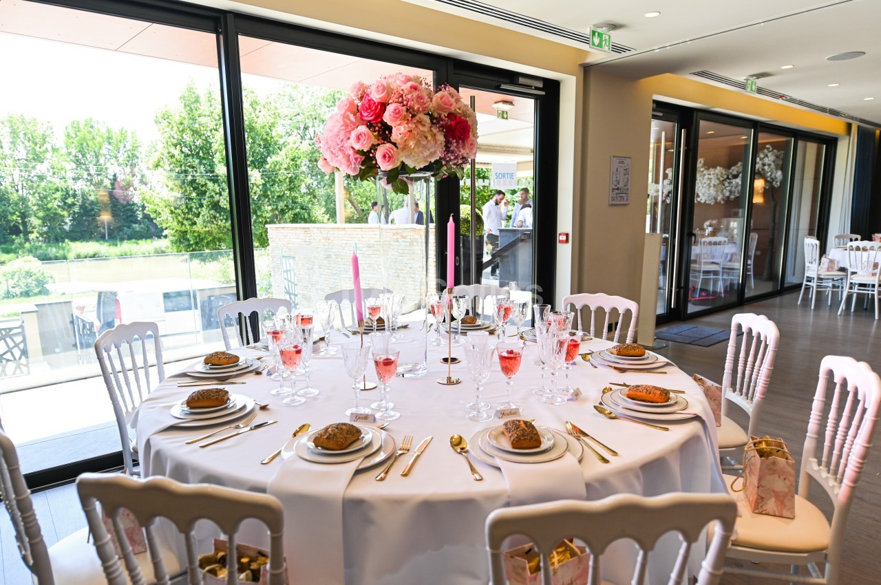 Table élégamment dressée avec nappes blanches, vaisselle dorée, verres à pied et centre de table floral rose.