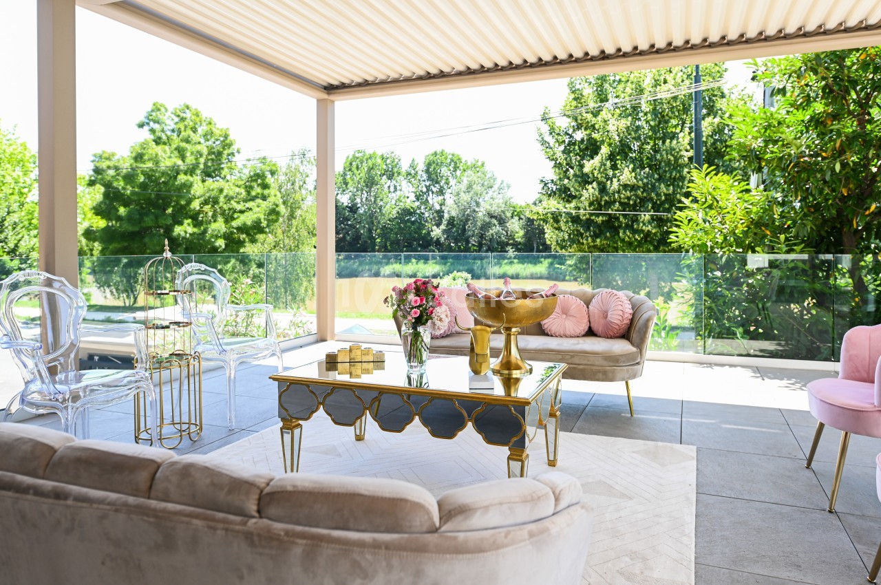 Terrasse aménagée avec mobilier élégant, table dorée, canapés clairs, et vue sur un jardin verdoyant.