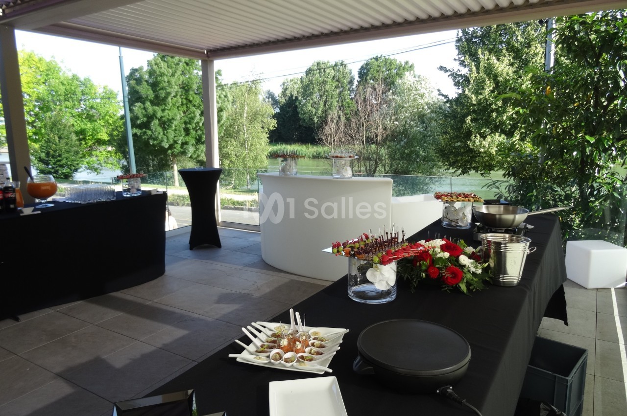 Table de buffet dressée avec des amuse-bouches, fleurs rouges et vue sur un espace extérieur verdoyant.