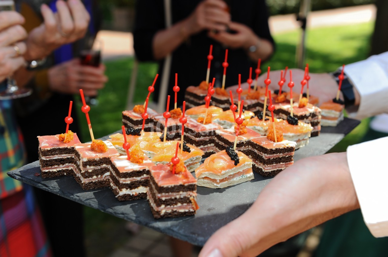 Plateau de canapés variés avec des brochettes rouges, tenu par une personne lors d'un événement en extérieur.