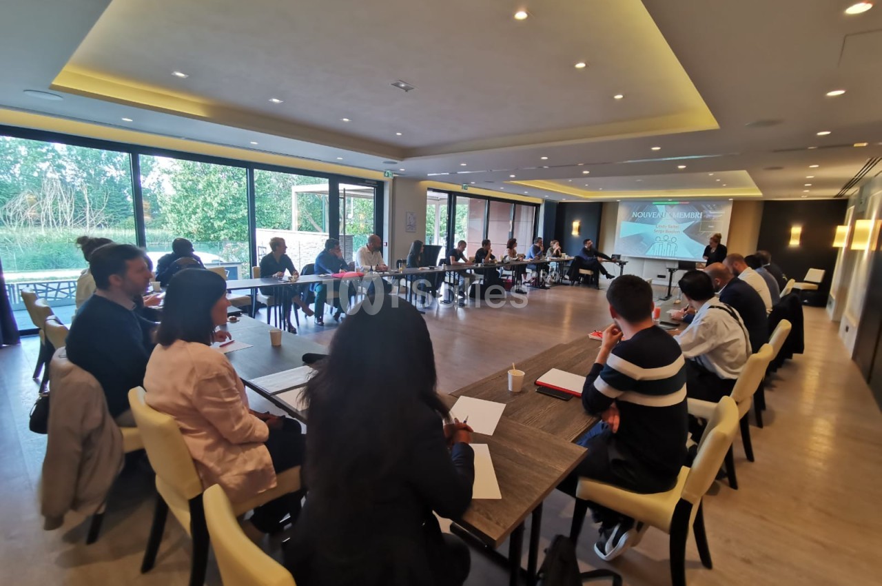 Des personnes assises autour d'une grande table en réunion dans une salle lumineuse avec vue sur l'extérieur.