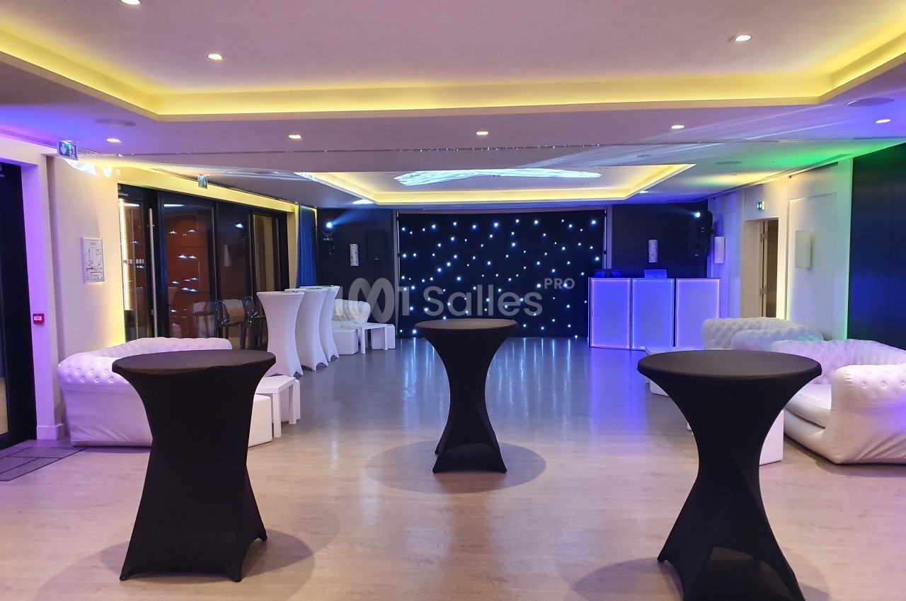 Salle de réception moderne avec tables hautes noires, canapés blancs et éclairage LED coloré.