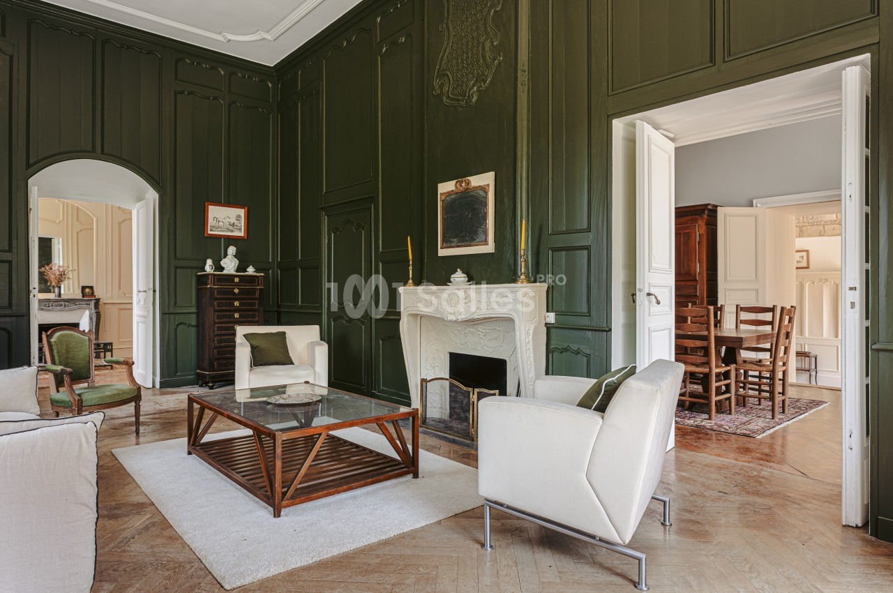 Salon élégant avec murs vert foncé, cheminée blanche sculptée, mobilier moderne et parquet en bois.