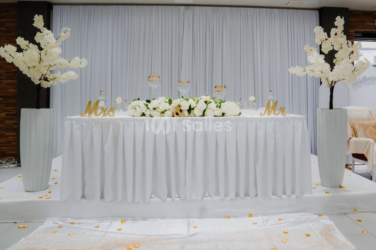 Table décorée pour un mariage avec nappes blanches, fleurs blanches, chandeliers et inscriptions ’Mrs’ et ’Mr’.