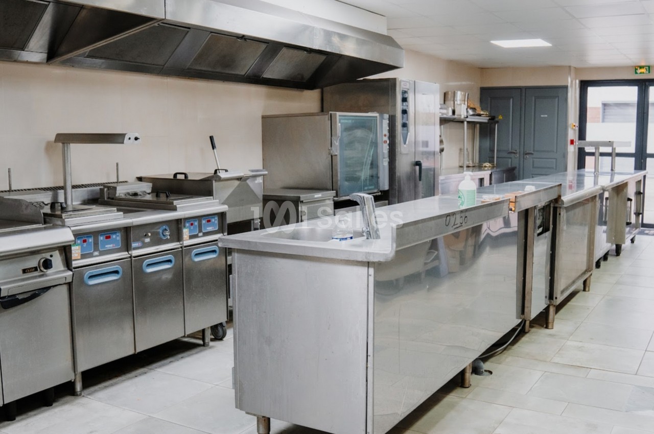 Cuisine professionnelle équipée avec plans de travail en inox, appareils de cuisson et hotte d'extraction.