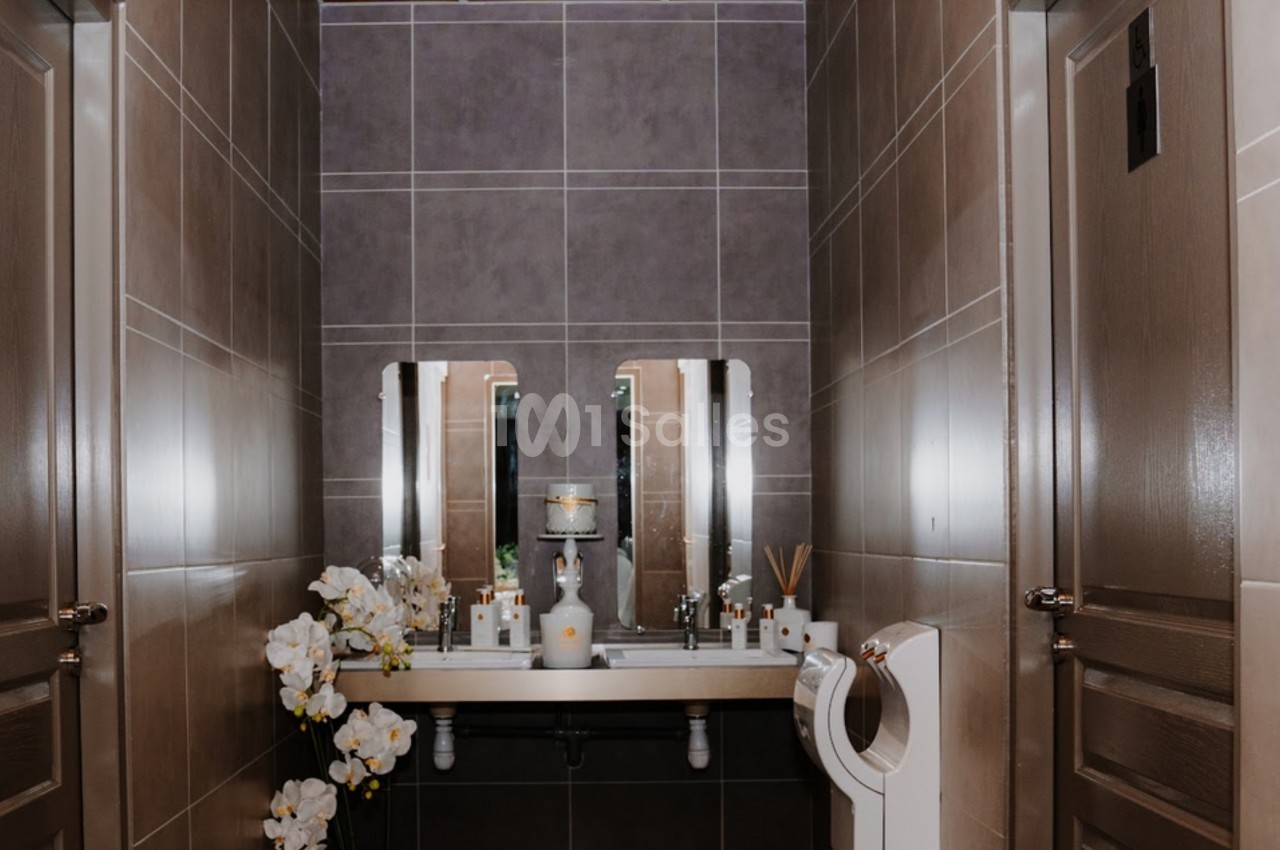 Salle de bain moderne avec deux miroirs, un lavabo double, des orchidées blanches et des murs carrelés beige.