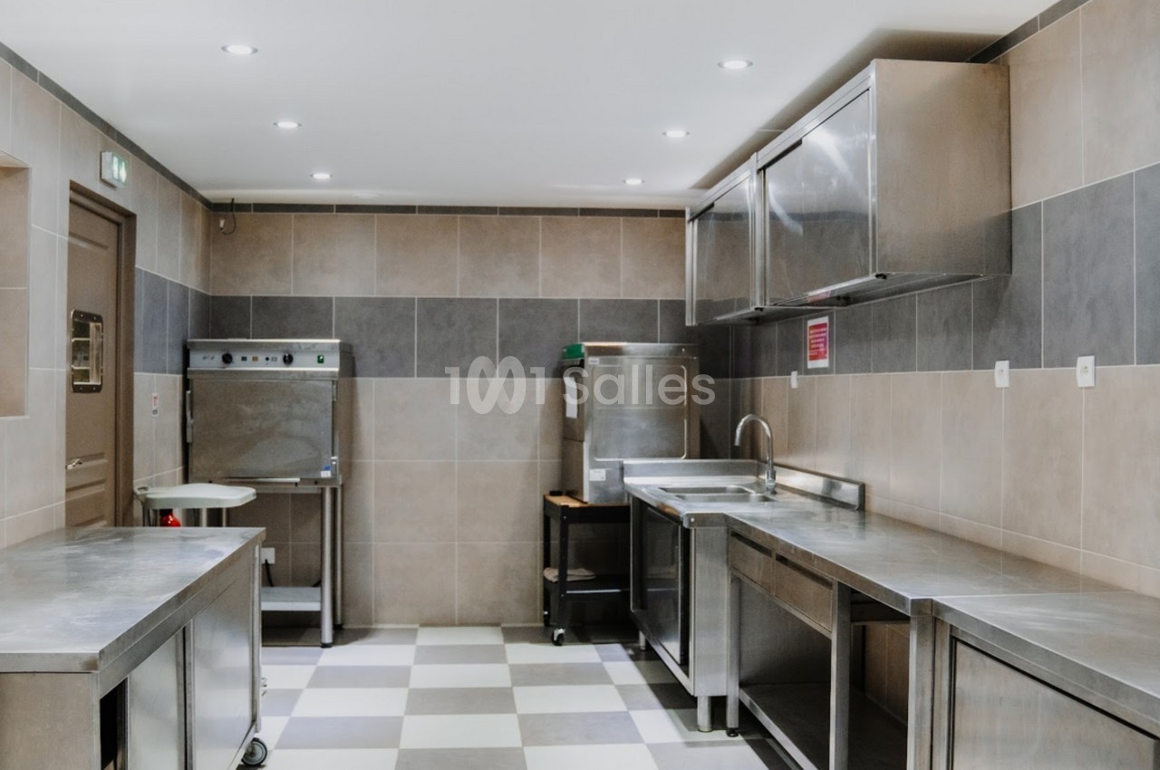 Cuisine professionnelle avec plans de travail en inox, carrelage au sol et équipements de restauration.
