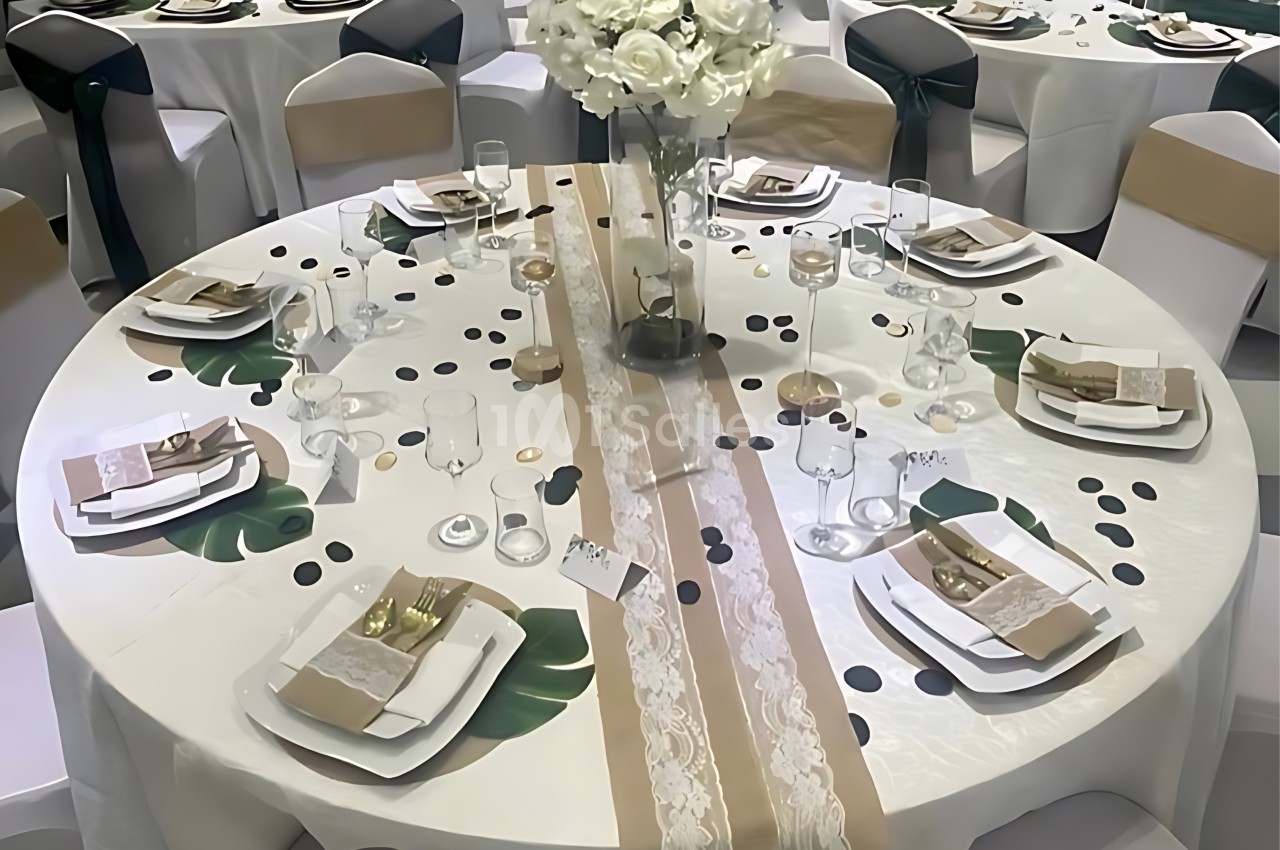 Table ronde décorée pour un événement, avec nappe blanche, chemins de table beige et blanc, et centre de table floral.