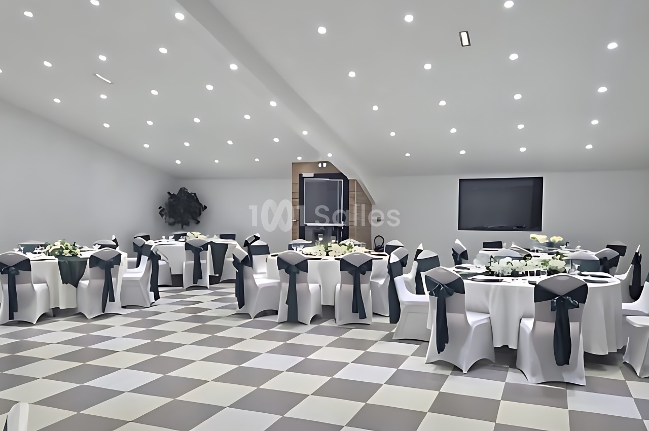 Salle de réception élégante avec tables rondes dressées, nappes blanches et chaises décorées de nœuds gris.