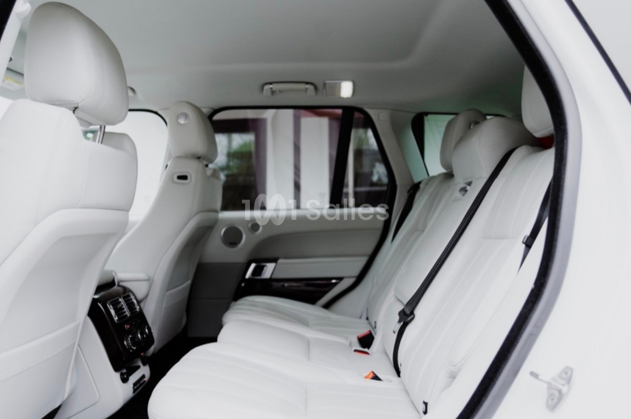 Intérieur d'une voiture avec des sièges arrière en cuir blanc, vue depuis une porte ouverte.