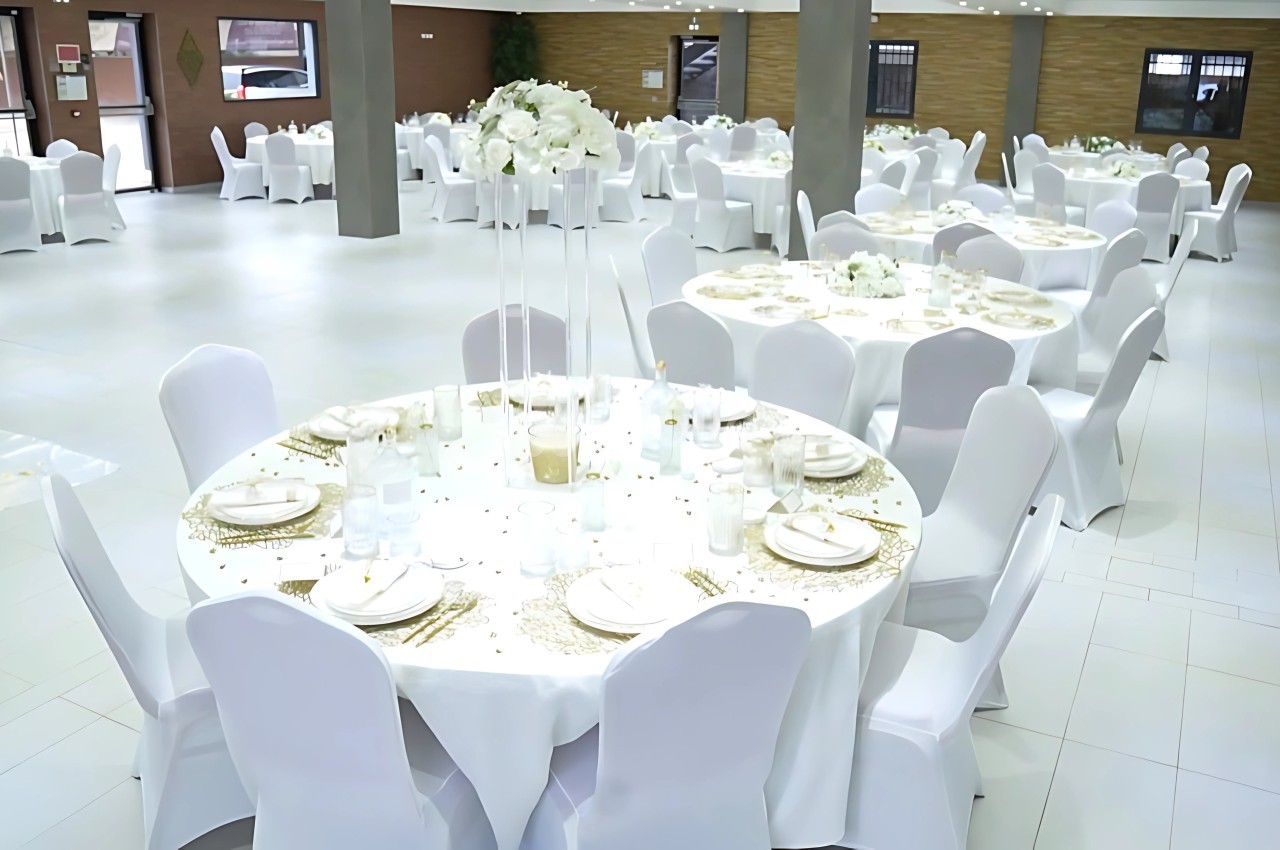 Salle de réception décorée avec des tables rondes dressées, nappes blanches et centres de table floraux.