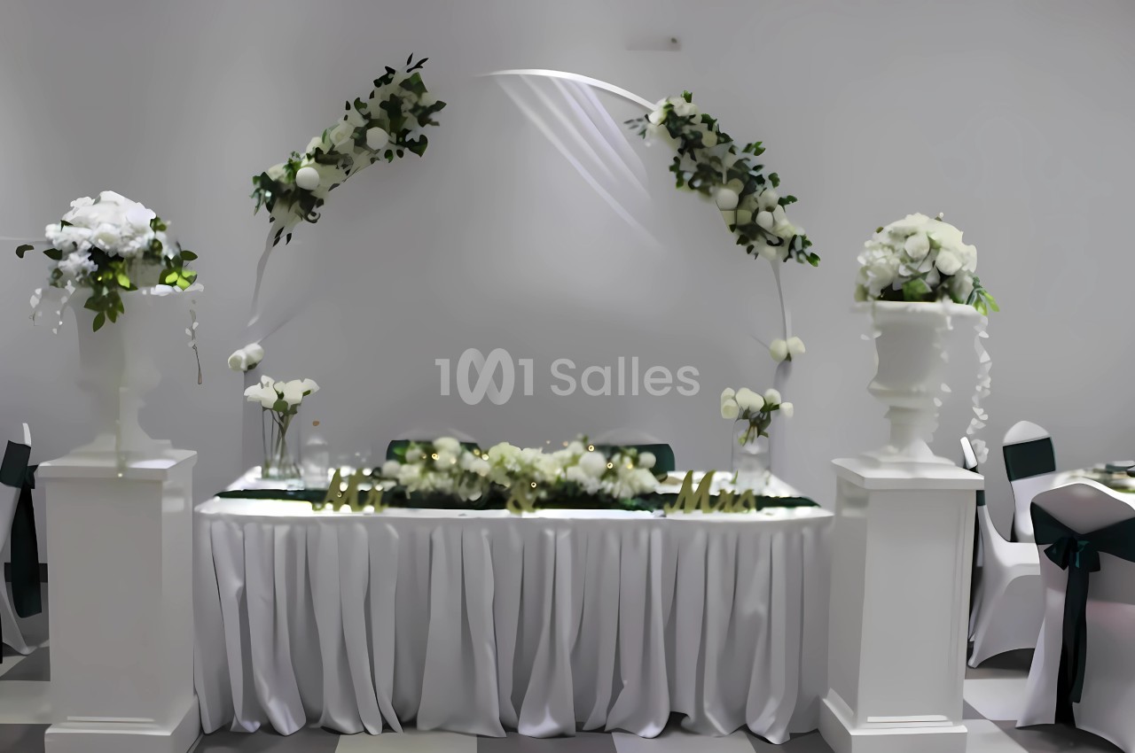Table décorée pour un mariage avec des fleurs blanches, un arche floral et des chaises habillées de housses.