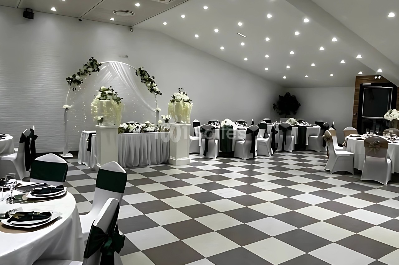 Salle de réception décorée pour un événement, avec tables dressées, chaises ornées et arche florale blanche.