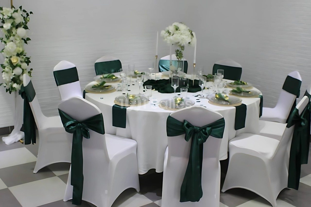 Table ronde décorée pour un événement, avec nappes blanches, chaises ornées de rubans verts et centre de table floral.