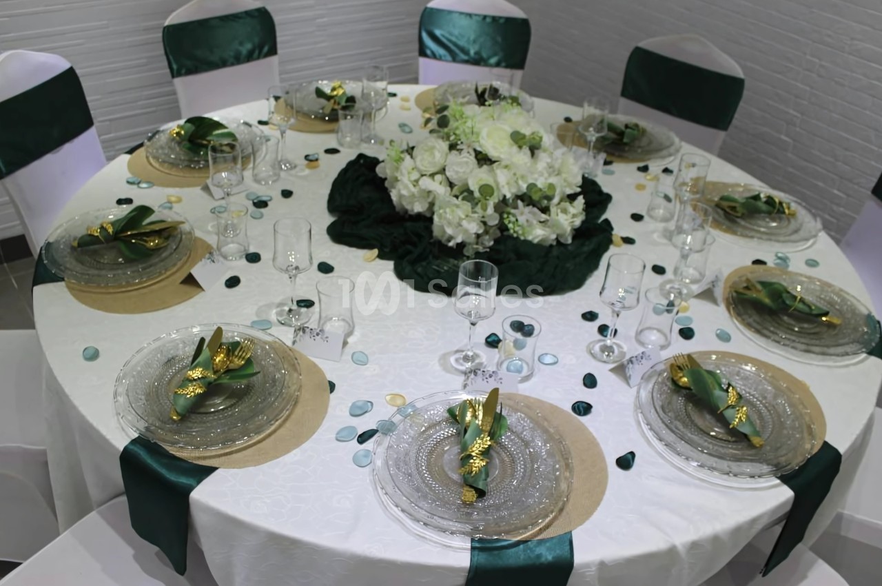 Table ronde élégamment dressée avec nappes blanches, serviettes vertes, vaisselle transparente et centre de table floral.