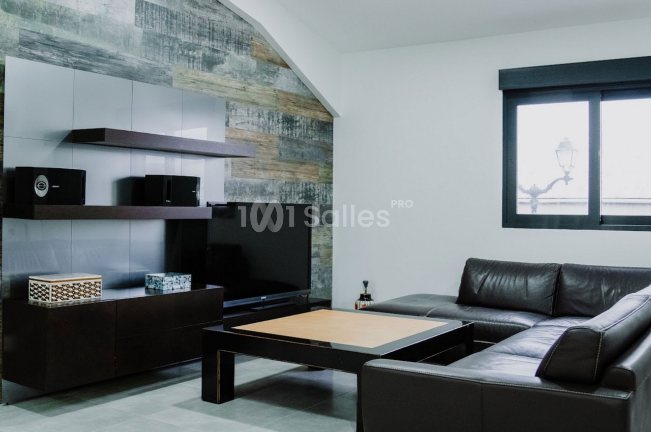 Salon moderne avec canapé en cuir marron, table basse en bois, étagères murales et grande fenêtre avec lumière naturelle.