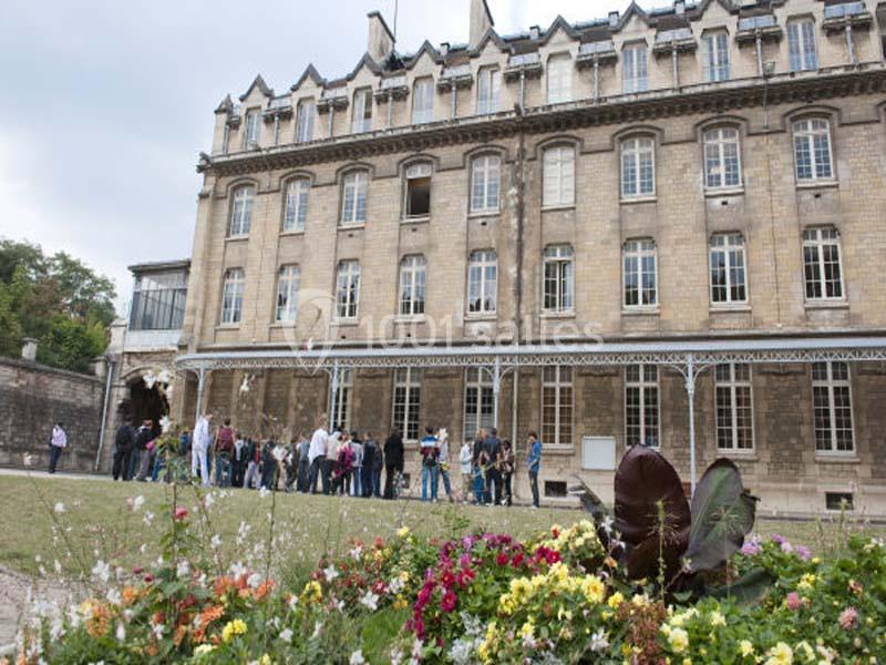 Groupe de personnes rassemblées devant un bâtiment ancien en pierre, avec des fleurs au premier plan.