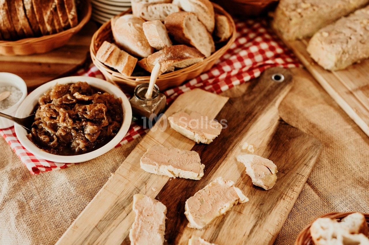 Tranches de foie gras disposées sur une planche en bois, entourées de pain et d'un bol de confit d'oignons.
