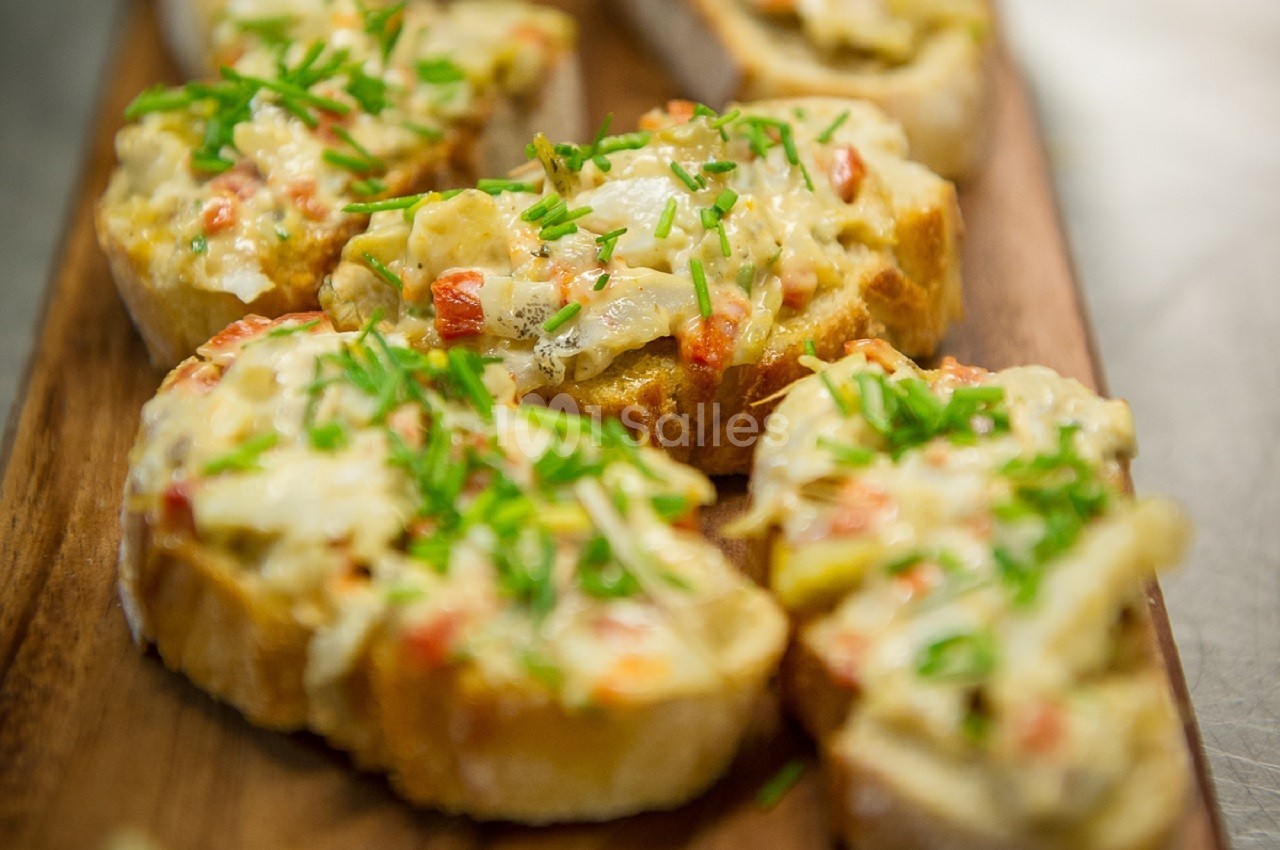 Tranches de pain garnies de fromage fondu, légumes et ciboulette, servies sur une planche en bois.