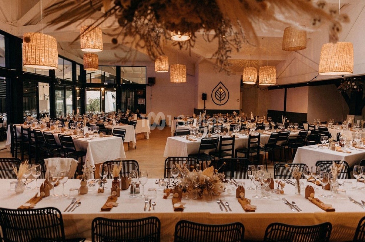 Salle de réception décorée avec des tables dressées, des chaises noires et des suspensions lumineuses en rotin.