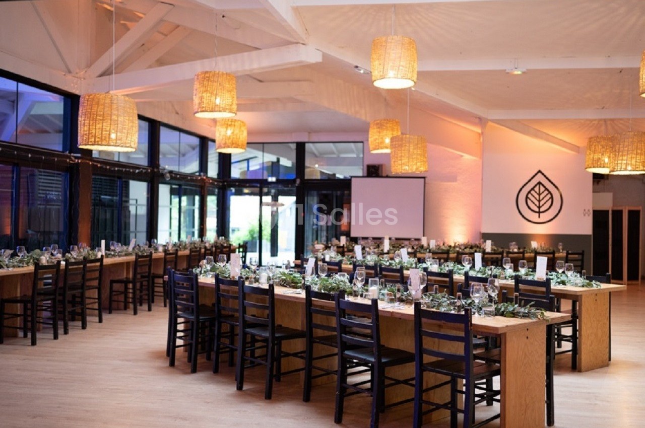 Salle de réception lumineuse avec de longues tables en bois décorées, éclairée par des suspensions en osier.