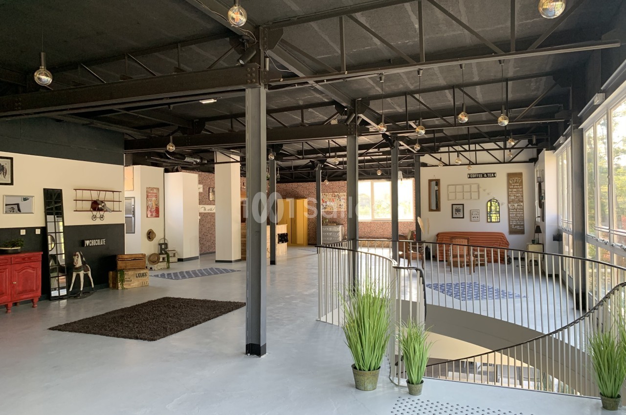 Intérieur spacieux et lumineux d'un loft industriel avec poutres métalliques, grandes fenêtres et décoration moderne.