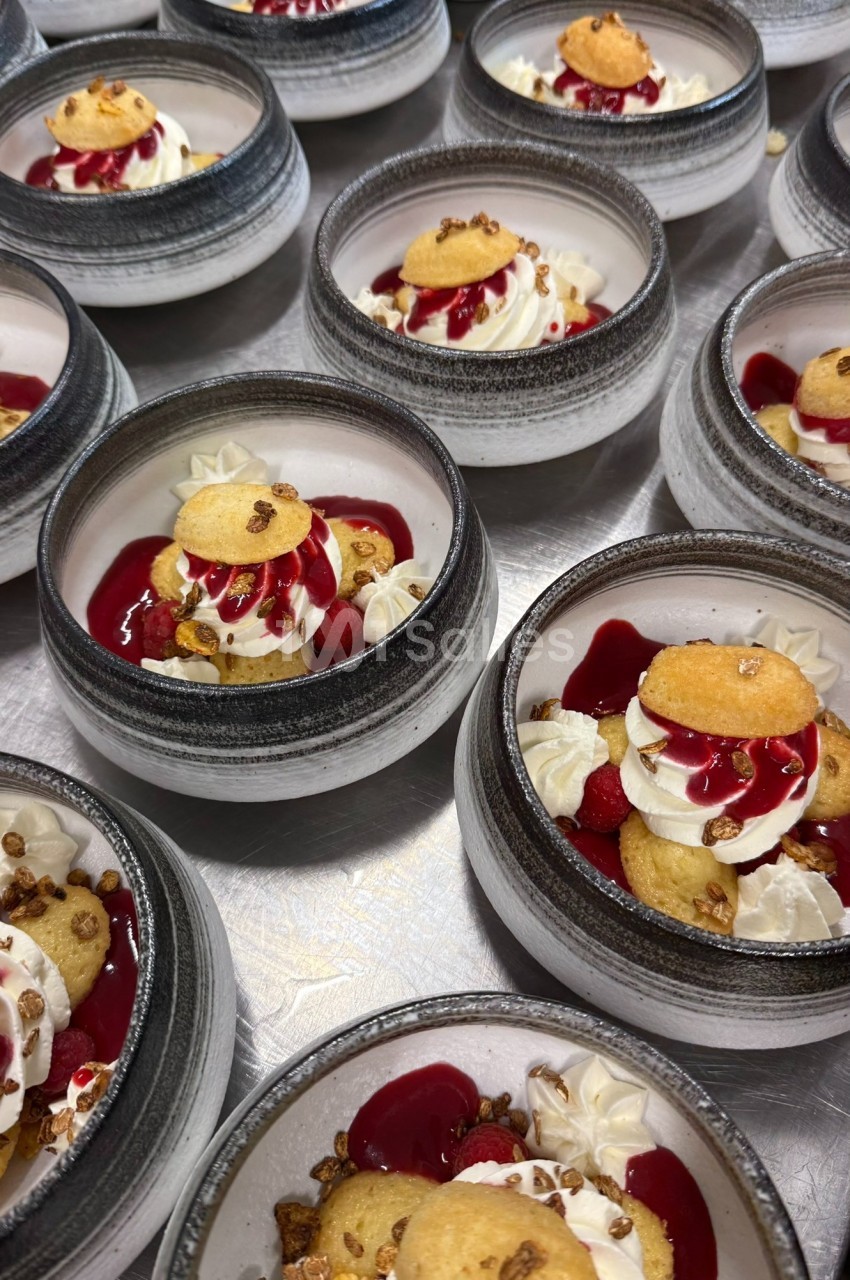 Desserts individuels dans des bols en céramique, composés de crème, coulis rouge, biscuits et éclats croustillants.