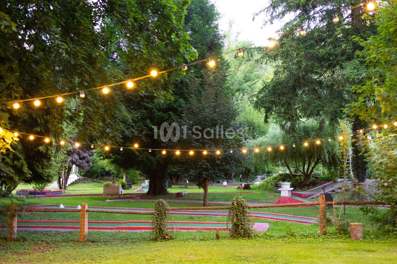 Terrain de mini-golf en extérieur entouré d'arbres, éclairé par des guirlandes lumineuses suspendues.