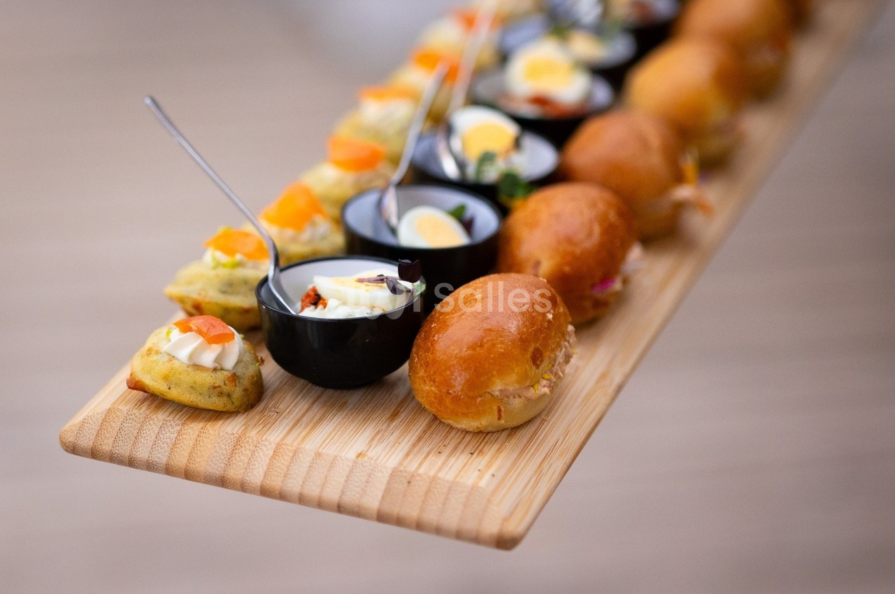 Plateau en bois avec un assortiment de bouchées salées, incluant mini-burgers, verrines et amuse-bouches variés.