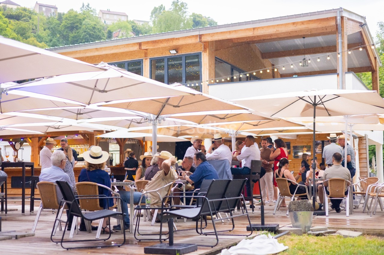 Personnes assises et debout sous des parasols sur une terrasse en bois devant un bâtiment moderne en bois.