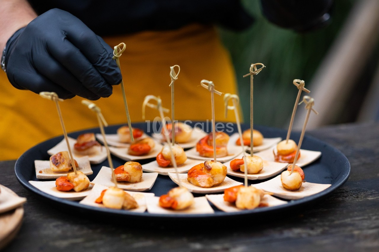 Un serveur dispose des amuse-bouches sur un plateau, chacun présenté sur une petite brochette en bois.