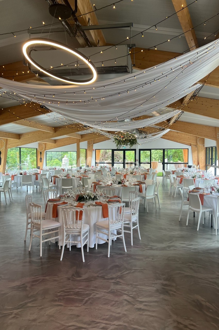 Salle de réception décorée avec des tables dressées, des nappes blanches et des guirlandes lumineuses suspendues.