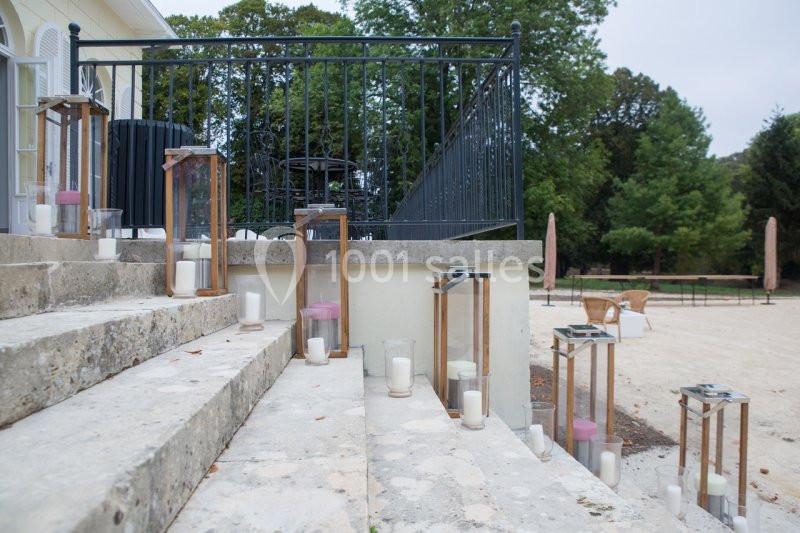 Bougies blanches et roses disposées dans des lanternes en bois sur des marches en pierre, près d'une rambarde en fer forgé.