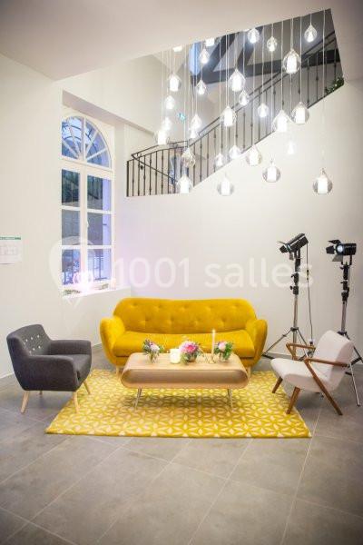 Salon moderne avec canapé jaune, fauteuils gris et blanc, table basse en bois, tapis à motifs et luminaires suspendus.