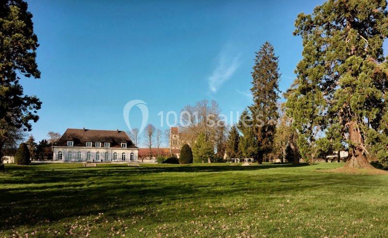 Parc verdoyant avec pelouse, grands arbres et un bâtiment ancien en arrière-plan sous un ciel dégagé.