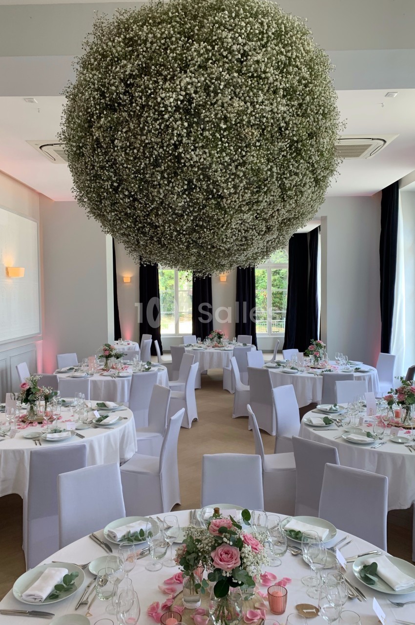 Salle de réception élégante avec tables décorées de fleurs roses et blanches, et une grande suspension florale.