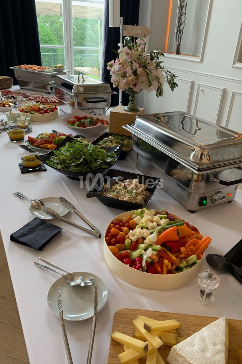 Buffet varié avec plats chauds en chafing dishes, salades, légumes frais, fromages et décoration florale.