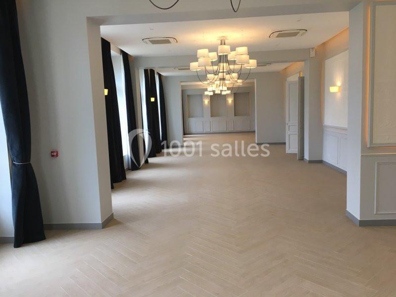 Salle lumineuse avec parquet clair, murs blancs, rideaux sombres et lustres modernes suspendus au plafond.