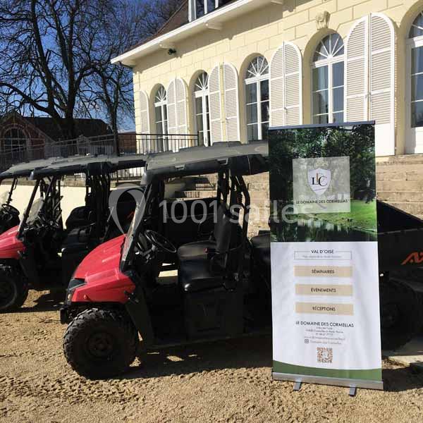 Deux véhicules tout-terrain rouges stationnés devant un bâtiment avec un panneau promotionnel à droite.
