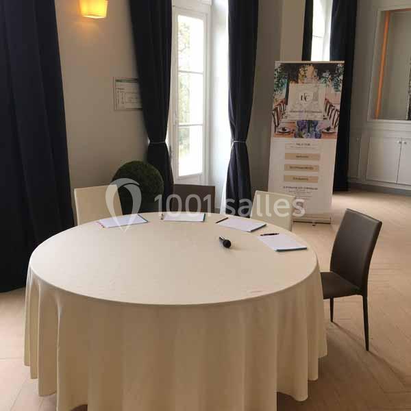 Table ronde couverte d'une nappe blanche avec quatre chaises, des documents et stylos, dans une salle lumineuse.