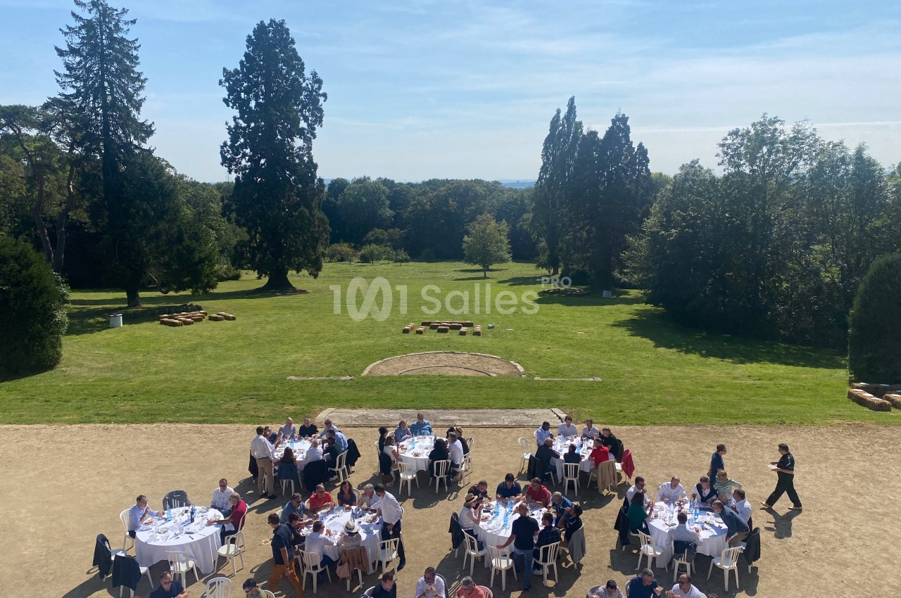 Personnes assises à des tables rondes en plein air dans un parc verdoyant sous un ciel dégagé.