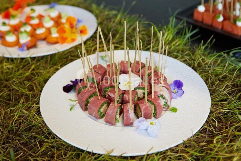 Assiette de bouchées apéritives à base de viande, présentées avec des fleurs comestibles sur un lit d'herbe.