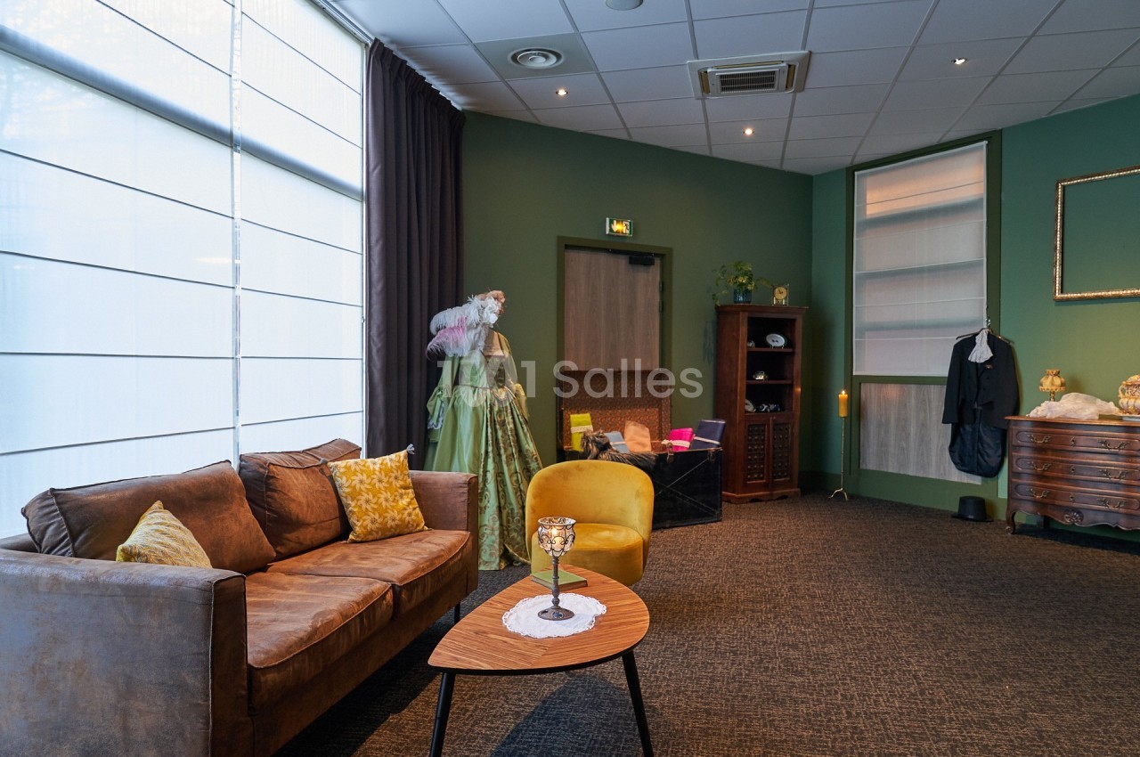 Salon aménagé avec canapé, fauteuil, table basse, armoire, et décorations, dans une pièce aux murs verts.