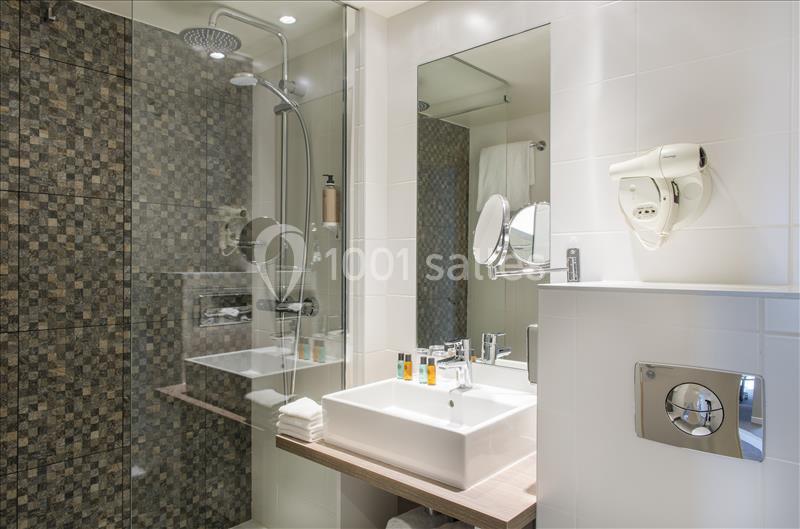 Salle de bain moderne avec douche à l'italienne, lavabo, miroir, sèche-cheveux mural et carrelage mosaïque.