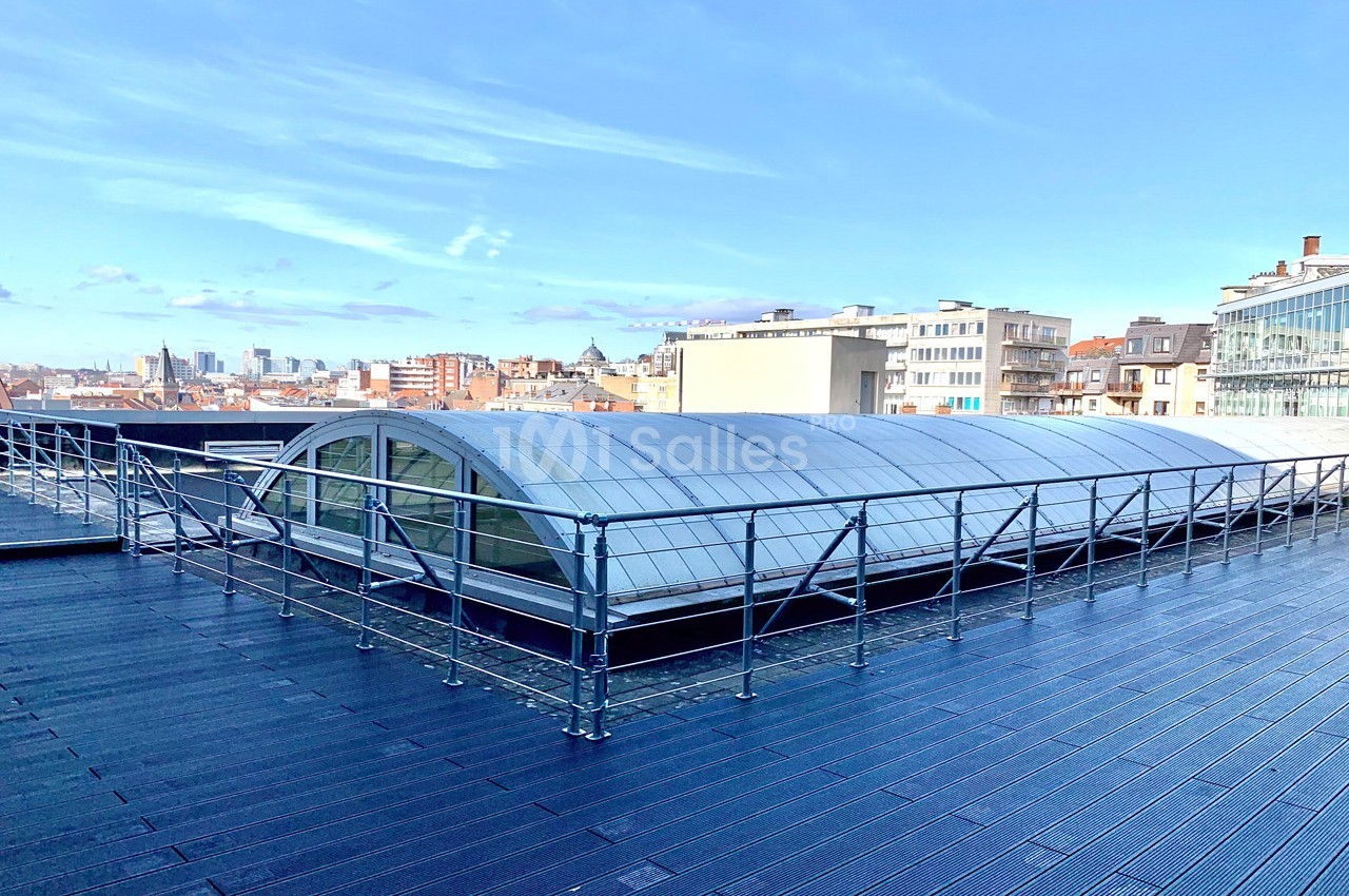 Toit-terrasse avec garde-corps, surface en bois et structure vitrée arrondie, vue sur des bâtiments urbains.