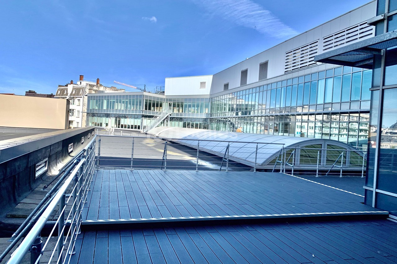 Vue d'une terrasse en bois surplombant un bâtiment moderne avec des façades vitrées sous un ciel bleu.