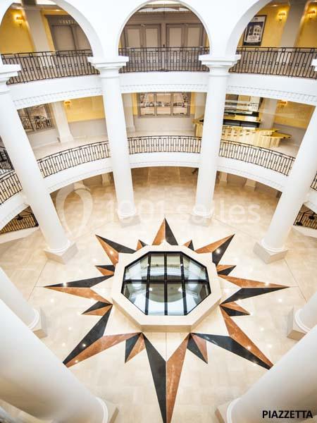 Vue intérieure d'un bâtiment avec un atrium circulaire, des colonnes blanches et un sol décoré d'une étoile géométrique.