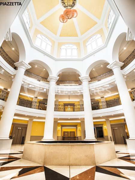 Intérieur d'un bâtiment avec une rotonde lumineuse, colonnes blanches et sol en marbre géométrique.