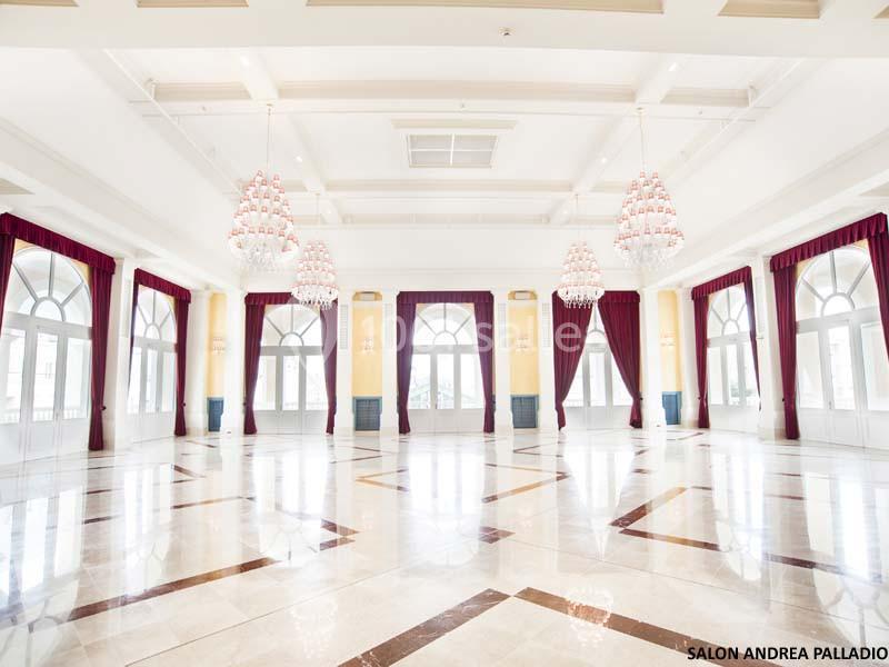 Salle spacieuse et lumineuse avec sol en marbre, grandes fenêtres voûtées, rideaux rouges et lustres imposants.