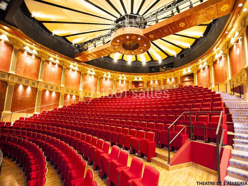 Salle de théâtre avec sièges rouges disposés en gradins, plafond orné et éclairage chaleureux.